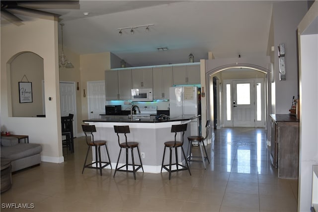 kitchen featuring sink, a kitchen breakfast bar, high vaulted ceiling, white appliances, and light tile patterned flooring