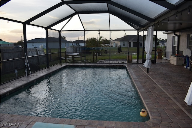 pool at dusk with glass enclosure and a patio area