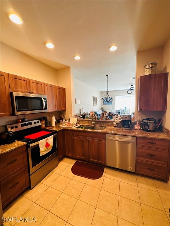 kitchen with stone counters, sink, decorative light fixtures, light tile patterned floors, and appliances with stainless steel finishes