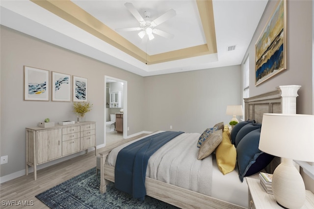 bedroom with hardwood / wood-style floors, a raised ceiling, ensuite bath, and ceiling fan