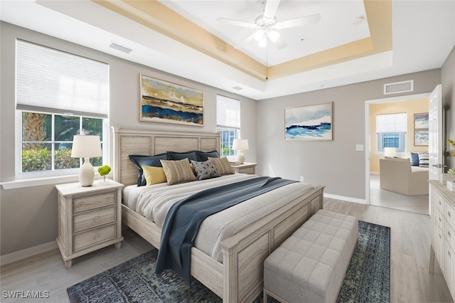 bedroom featuring ceiling fan, light hardwood / wood-style floors, a tray ceiling, and multiple windows