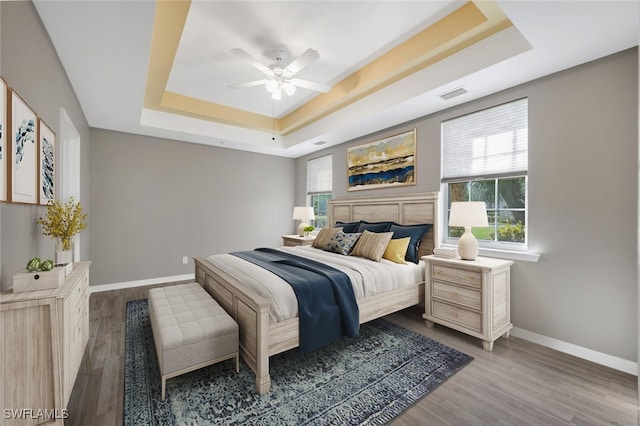 bedroom with wood-type flooring, ceiling fan, and a tray ceiling