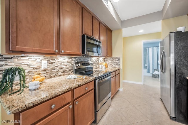 kitchen featuring tasteful backsplash, light stone counters, light tile patterned floors, and appliances with stainless steel finishes