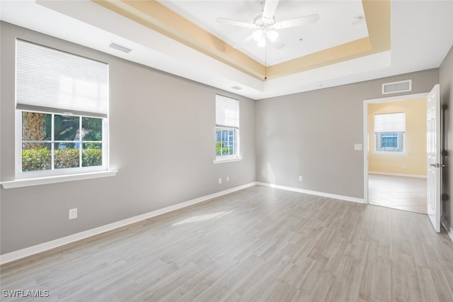 spare room with a raised ceiling, ceiling fan, and light wood-type flooring