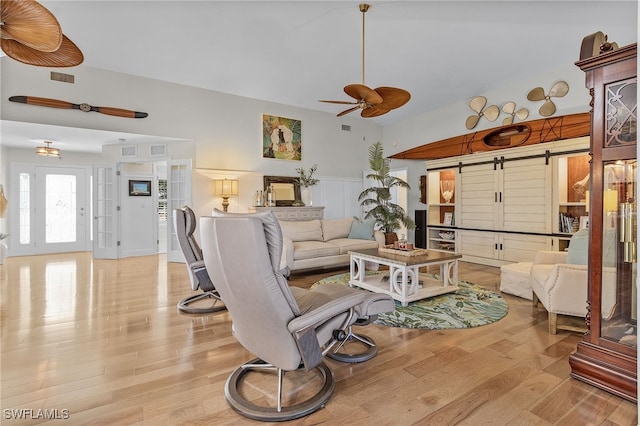 living room with light wood-type flooring, a barn door, and ceiling fan