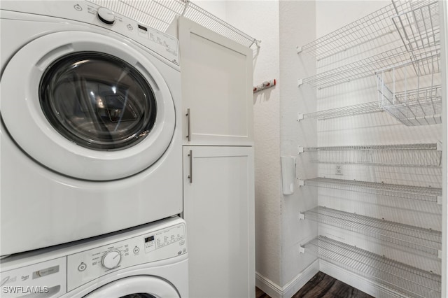 washroom with dark hardwood / wood-style flooring, stacked washer and dryer, and cabinets