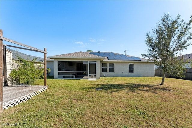 rear view of house with a sunroom, solar panels, a wooden deck, and a lawn