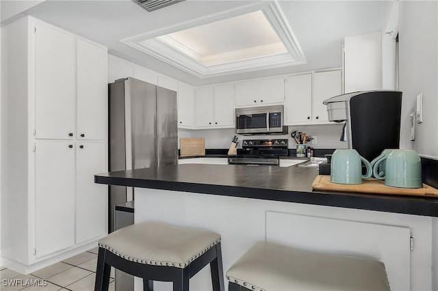 kitchen featuring kitchen peninsula, appliances with stainless steel finishes, a kitchen breakfast bar, a raised ceiling, and white cabinetry