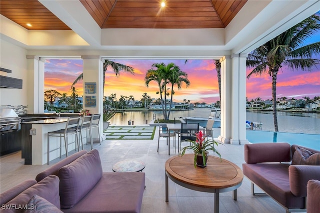 patio terrace at dusk featuring outdoor lounge area, a water view, a grill, a bar, and exterior kitchen