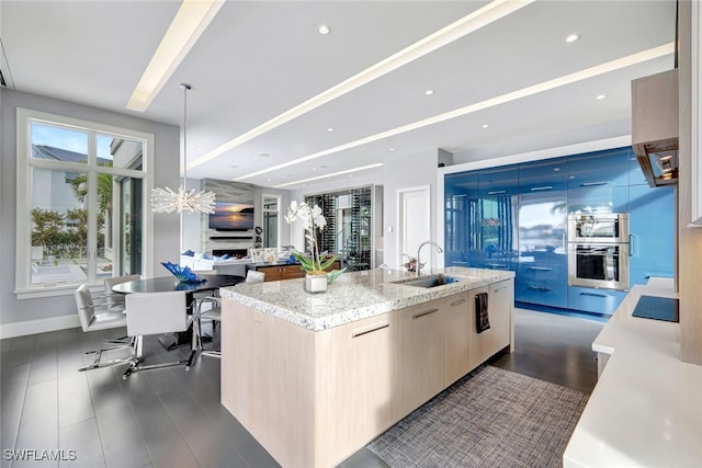 kitchen featuring light brown cabinetry, sink, an island with sink, light stone countertops, and oven