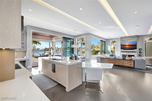 kitchen featuring a kitchen bar, sink, light stone counters, decorative light fixtures, and an island with sink