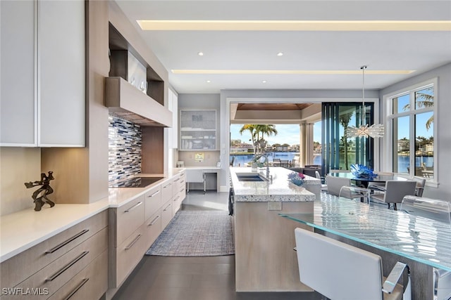 kitchen featuring pendant lighting, tasteful backsplash, sink, black electric stovetop, and wall chimney range hood