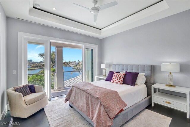 bedroom featuring a water view, access to exterior, ceiling fan, and a tray ceiling