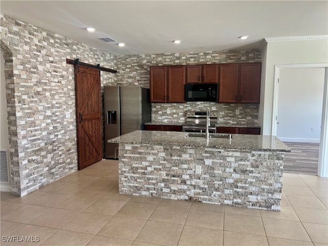 kitchen with light stone countertops, a barn door, stainless steel appliances, and a center island with sink