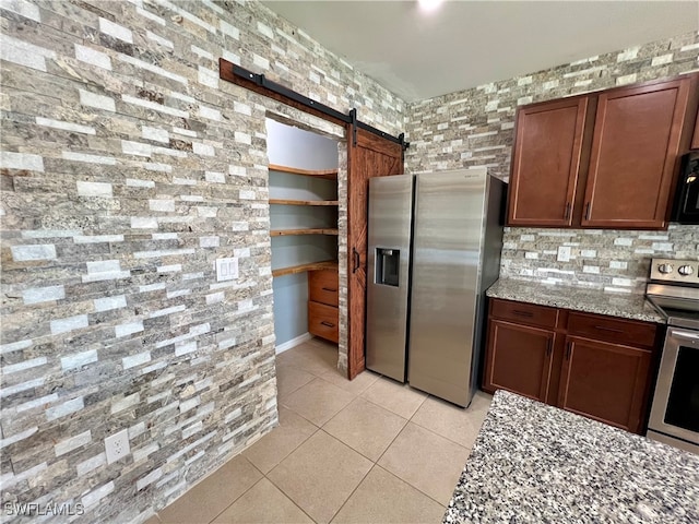 kitchen featuring a barn door, light stone counters, light tile patterned floors, and stainless steel appliances