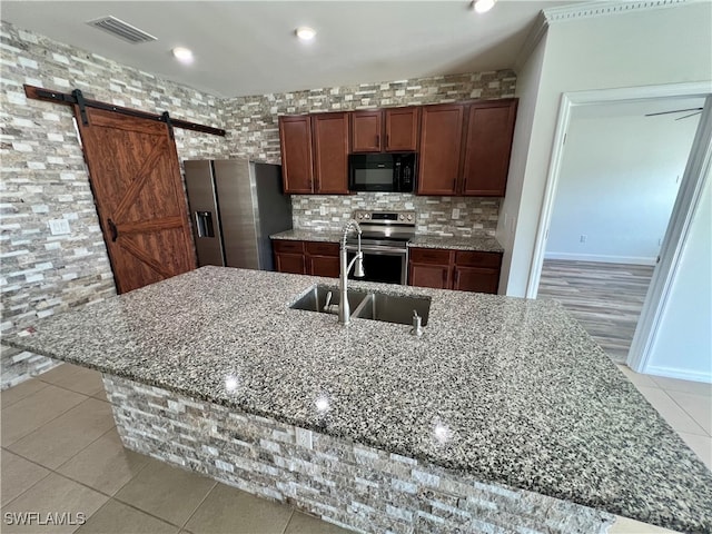 kitchen with light stone countertops, sink, stainless steel appliances, a barn door, and a center island with sink