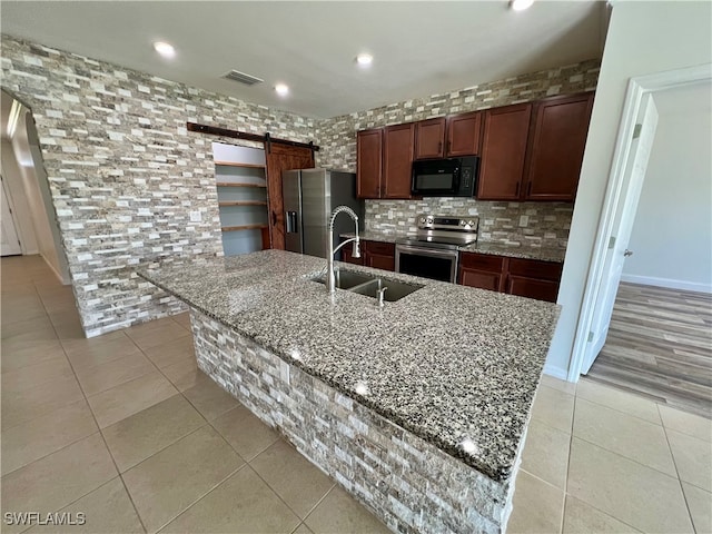 kitchen featuring a barn door, a kitchen island with sink, sink, and appliances with stainless steel finishes