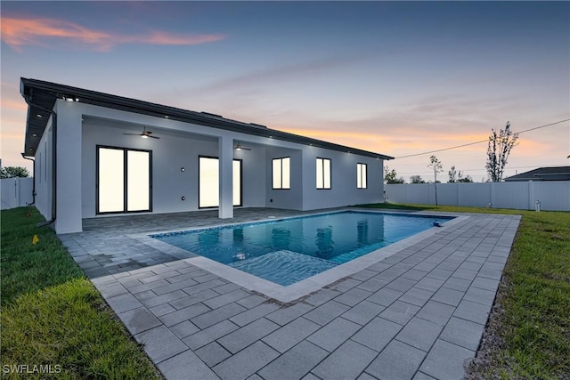 pool at dusk with a patio, ceiling fan, and a lawn