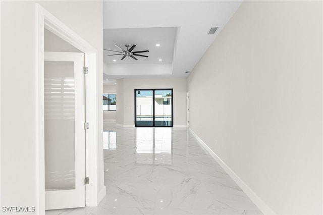 empty room with ceiling fan and a raised ceiling