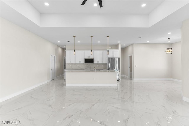 kitchen with pendant lighting, a large island, stainless steel refrigerator, ceiling fan, and white cabinetry