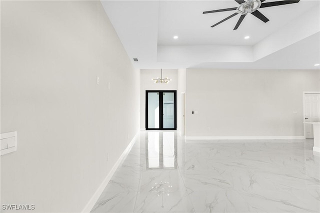 spare room featuring a raised ceiling and ceiling fan with notable chandelier