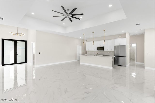 unfurnished living room with a tray ceiling, ceiling fan with notable chandelier, and french doors