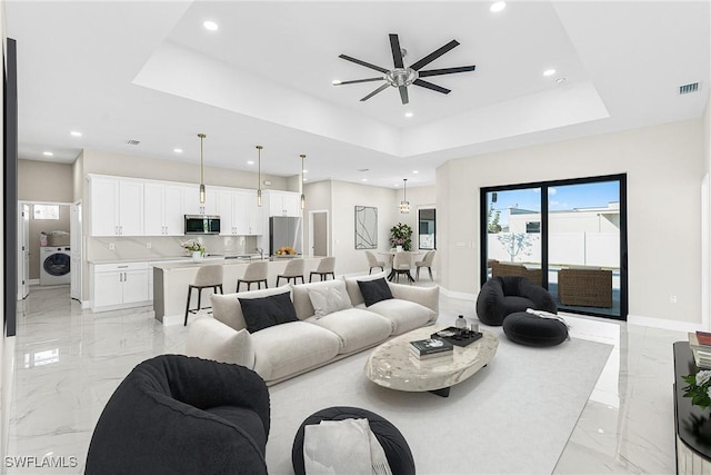 living room with washer / dryer, a raised ceiling, and ceiling fan