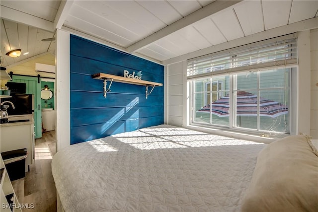 bedroom with sink, a barn door, lofted ceiling with beams, wooden walls, and hardwood / wood-style flooring