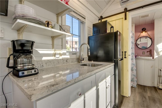 kitchen with white cabinetry, sink, light stone countertops, a barn door, and lofted ceiling