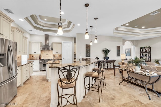 kitchen featuring a raised ceiling, dark stone countertops, wall chimney range hood, and appliances with stainless steel finishes