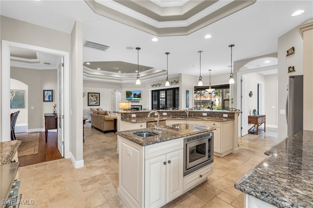 kitchen with stainless steel appliances, a large island with sink, crown molding, dark stone counters, and decorative light fixtures