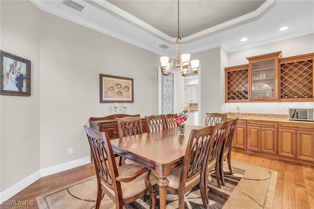 dining room featuring a tray ceiling, ornamental molding, a notable chandelier, and light wood-type flooring