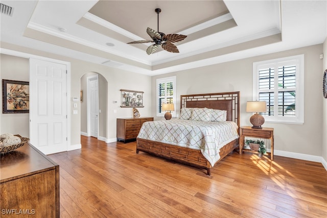 bedroom with ceiling fan, wood-type flooring, crown molding, and a tray ceiling