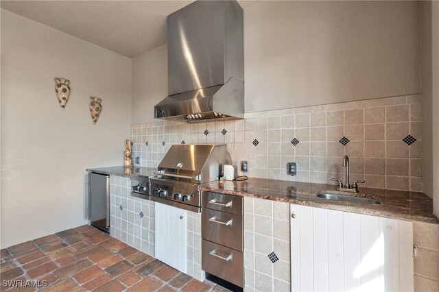 kitchen featuring decorative backsplash, stainless steel fridge, sink, wall chimney range hood, and dark stone countertops