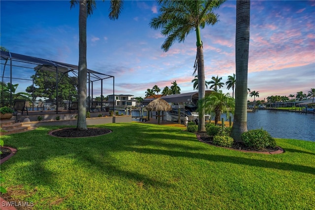 yard at dusk with a boat dock, a water view, and a lanai