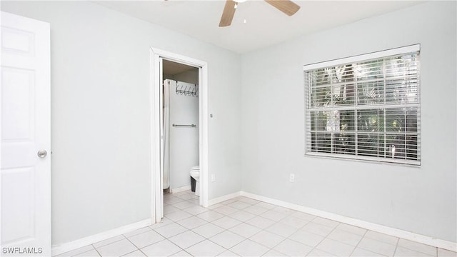 unfurnished bedroom featuring ensuite bath, ceiling fan, light tile patterned floors, and a spacious closet