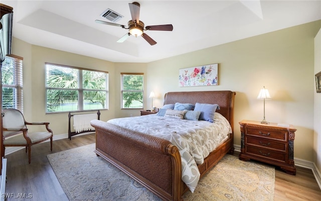 bedroom with hardwood / wood-style floors, a tray ceiling, and ceiling fan