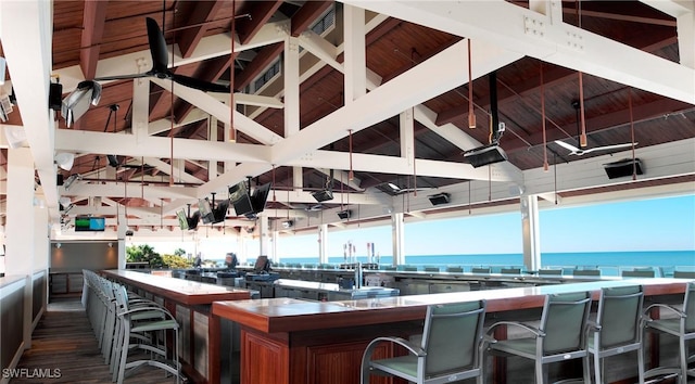 interior space with high vaulted ceiling, a water view, dark hardwood / wood-style floors, beamed ceiling, and a kitchen bar