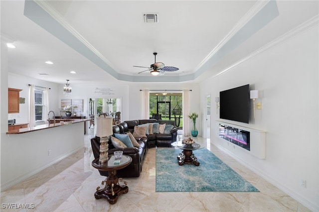 living room featuring a glass covered fireplace, a tray ceiling, crown molding, and visible vents