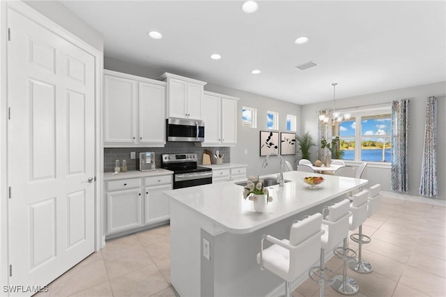 kitchen featuring appliances with stainless steel finishes, decorative light fixtures, a center island with sink, and white cabinets