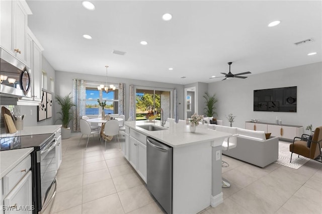 kitchen with appliances with stainless steel finishes, decorative light fixtures, white cabinetry, sink, and a center island with sink