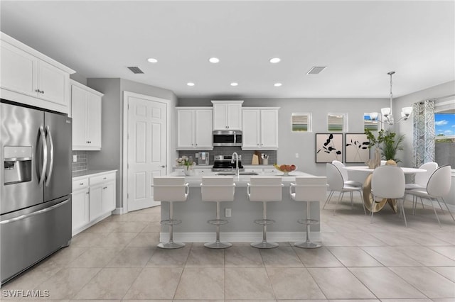 kitchen with stainless steel appliances, white cabinetry, sink, and a center island with sink