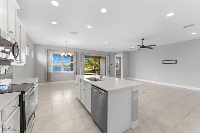 kitchen with sink, appliances with stainless steel finishes, an island with sink, white cabinets, and ceiling fan with notable chandelier