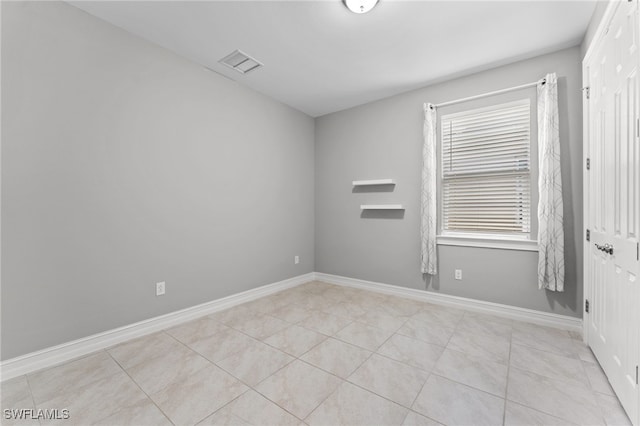 spare room featuring light tile patterned floors, visible vents, and baseboards