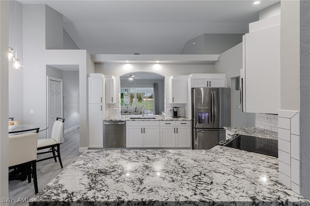 kitchen with decorative backsplash, light stone counters, stainless steel appliances, ceiling fan, and white cabinets