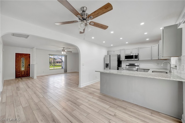 kitchen featuring sink, light hardwood / wood-style flooring, light stone countertops, kitchen peninsula, and stainless steel appliances