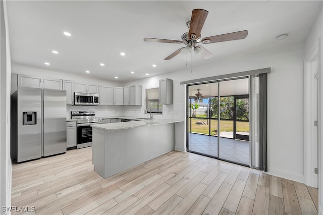 kitchen featuring ceiling fan, tasteful backsplash, light hardwood / wood-style flooring, kitchen peninsula, and appliances with stainless steel finishes