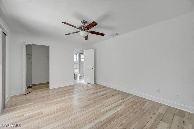 unfurnished bedroom with a walk in closet, light wood-type flooring, ensuite bath, ceiling fan, and a closet