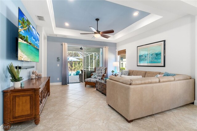 tiled living room with ceiling fan and a tray ceiling