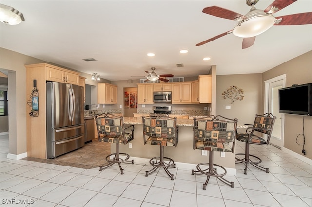 kitchen with a breakfast bar, light stone countertops, light brown cabinetry, light tile patterned flooring, and stainless steel appliances